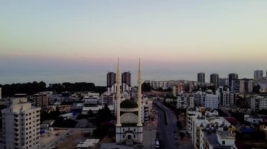 Gün batımında denizin arka planına karşı şehir merkezinde iki minaresi olan küçük bir cami. Silah bir İHA 'dan ateşlenmiş. İki minaresi olan bir camiden uzaklaşıyor. İslam kavramı.