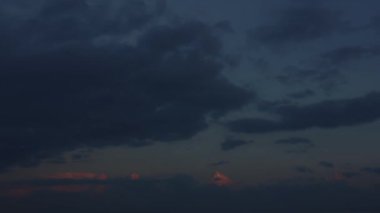 Akşam vakti gökyüzü hızlanırken, büyüleyici bir bulut bulutu zıt yönlerde yatay hareket ederek bulutlu günbatımının arka planına karşı büyüleyici bir tablo çizer..
