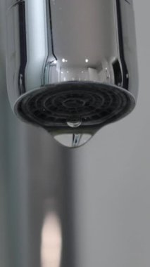 Metal su musluğunun beyaz arka plandaki aşırı yakın çekimi izole edilmiş. Düşen damlalar yavaş çekimde can sıkıcı oluyor. Yüksek kalite 4k görüntü