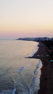 İnsansız hava aracı günbatımında kıyı manzarası sergiliyor. Akşam ışığı kıyı manzarasını güzelleştirir. Sakin kıyı manzarası, denizin hareketli bir kasabayla buluştuğu yer..