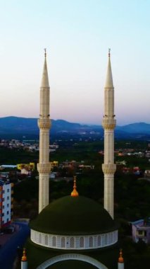 Gün batımında denizin arka planına karşı şehir merkezinde iki minaresi olan küçük bir cami. Silah bir İHA 'dan ateşlenmiş. İki minaresi olan bir camiden uzaklaşıyor. İslam kavramı.