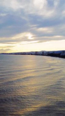 Drone gün batımında deniz kenarı kıyılarında dalgalar olduğunu gösteriyor. İnsansız hava aracı, sakin günbatımını kıyı boyunca yakalar, dalgalar yavaşça hareket eder. Deniz kenarı kasabaları gün batımında güzellik, drone tarafından çekilen dalgalar. Yüksek kalite 4k görüntü