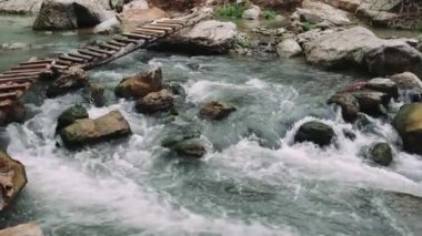Tahta köprü dağ deresini geçiyor, manzaralı bir manzara. Dağ deresi, ahşap köprünün altında kıvrılır. Huzurlu güzellik. Dağ deresinin üzerindeki ahşap köprü, huzur dolu keşiflere davetiye çıkarıyor..