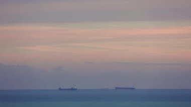 Akdeniz kıyıları Mersin, Türkiye 'de, gün batımında kargo gemileriyle demirli. Akşam gökyüzüne karşı gemi siluetleri, iskele girişini bekliyor. Günbatımında Türk kıyı şeridi yakınlarında gemi manzarası.