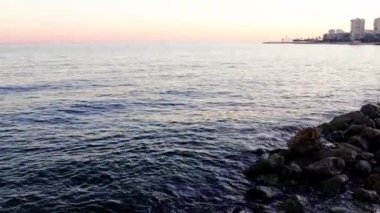 Akdeniz şehri gün batımında ufuk çizgisi, sakin deniz suyu şehir ışıklarını yansıtıyor. Gün sona ererken Akdeniz 'in huzurlu manzarası. Akdeniz yakınlarında sakin bir deniz alacakaranlıkta. Yüksek kalite 4k görüntü