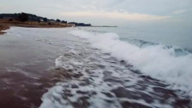 Drone gün batımında kumsalda alçaktan süzülür, canlı denizi ortaya çıkarır, sörf yapar. Büyüleyici deniz manzarası, sörf. Çarpıcı deniz, sörf, kıyı boyunca dalgalar. Yüksek kalite 4k görüntü