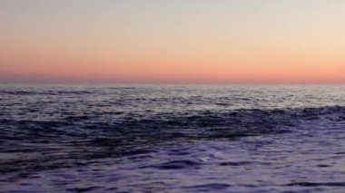 Gün batımında kumlu kumsalda dalgalar peş peşe geliyor. Her dalga sakin plaj akşamlarının özünü yakalıyor. Sahili saran ritmik dalgalarla gün batımı sahnesi. Yüksek kalite 4k görüntü