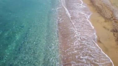 Drone görüntüsü sahil boyunca dalgaları yakalar, kumlu sörfün denizle buluşmasını. Kumsallar dalgaları selamlar, tepemizde insansız hava aracı. Deniz dalgaları kumsala çarpıyor, İHA havada süzülüyor. Yüksek kalite 4k görüntü
