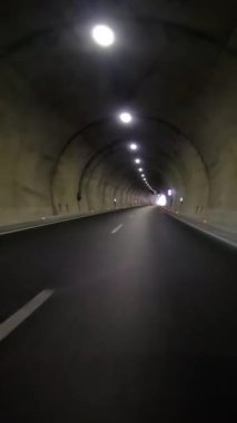 Araba tünelden çıkıyor, karayolu karanlığını açığa çıkarıyor. Arabadaki görüntüler tünel çıkışını gösteriyor, arabayı vurguluyor, tünel geçişini gösteriyor..