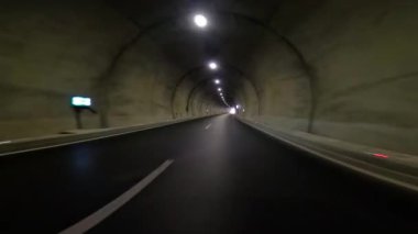 Araba tünelden çıkıyor, karayolu karanlığını açığa çıkarıyor. Arabadaki görüntüler tünel çıkışını gösteriyor, arabayı vurguluyor, tünel geçişini gösteriyor..