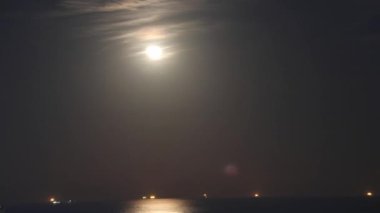 Dolunay yükseliyor, dolunay, bulut, deniz geceleri kucaklaşıyor. Sahne, kıyı kenti üzerinde ay, bulut ve deniz gösteriyor. Gemiler ay, bulut ve deniz gökyüzüne hükmederken ışıldıyor. Yüksek kalite 4k görüntü