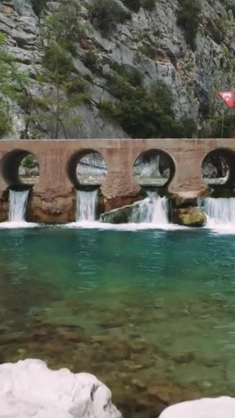 ドローンは岩の山の流れに架かる橋を捕獲する 明確な水が橋の下に流れ 風光明媚な設定になっています 空中ビューは 高速ストリームを横断する橋をハイライトします 高品質の4K映像 — ストック動画