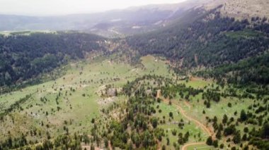 Hava manzarası, orman ortamındaki dağları, yemyeşil toprak yolu takip eder. İnsansız hava aracı görüntüleri manzarayı, kıvrımlı yolu olan dağları vurguluyor.