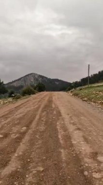 Dolambaçlı toprak bir yol, heybetli bir dağ manzarasının içinden geçiyor. Huzurlu ve büyüleyici bir yolculuk sunuyor..