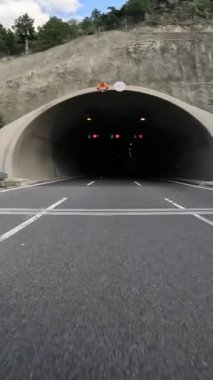 Dağlarda tünele giren ilk kişi görüldü. Araba tünele yaklaşırken sürüş başlıyor, açık yoldan tünele geçiş gösteriliyor. Dağ yolculuğu mühendislik harikasını vurguluyor. .