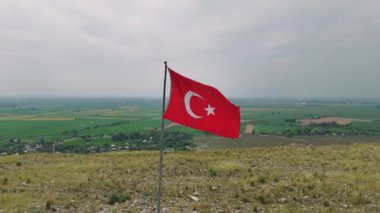 Beyaz yıldızlı canlı bir kırmızı bayrak ve yemyeşil bir vadiye bakan tepede gururla dalgalanan hilal..