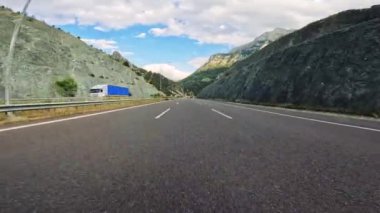 Bir araba bu manzaralı yolculukta nefes kesici bir dağ arkaplanı ile geniş bir açık yolda yol alır..