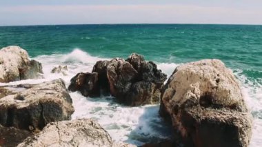 Serene Dancing: Turkuaz Dalgalar üzerinde dengelenen kayalar, bir grup kayanın, denizin her çarpışında nazikçe sallanan titreyen turkuaz dalgaların üzerinde hassas bir şekilde dengede durmasını sağlıyor. Yüksek kalite 4k görüntü