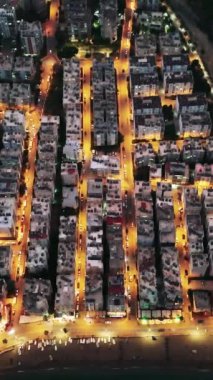 Türkiye 'nin Mersin kentinin günbatımından sonra çekilmiş büyüleyici hava görüntüsü. İnsansız hava aracının şehrin üzerinde yükselişini, aydınlık sokaklarının ve binalarının güzelliğini gösterişini izleyin..