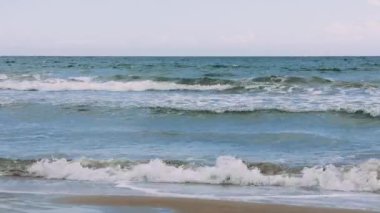 Gün batımında kumlu bir sahilde usulca dalgaların dalgalandığı sakin bir görüntü..