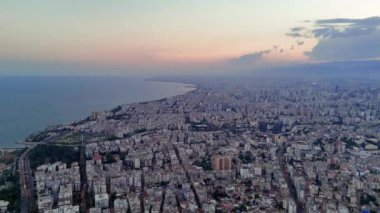 Güneş batarken bir dron kıyı kasabasının üzerinde uçuyor, suyun ve binaların üzerine altın bir parıltı saçıyor..