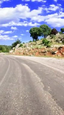 Nefes kesici bir dağ manzarasında nefes kesici bir yolculuğa çıkın. Pürüzsüz asfalt rüzgarları yemyeşil yeşil gökyüzünün altında dağınık beyaz bulutlar altında