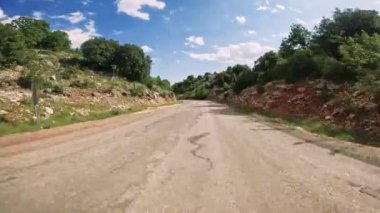 Resimli kırsal alanlarla çevrili sakin bir kırsal yol keşfedin. Yeşil manzaralar. Ve bulutlu açık mavi gökyüzünün altındaki kayalık tepeler. Doğanın güzelliğinde huzurlu bir yolculuğun tadını çıkar.