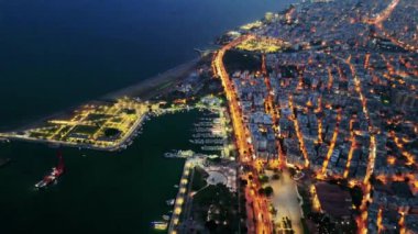 Bir İHA gece bir sahil kasabasında uçar, şehrin büyüleyici ışıklarını yakalar ve suya yansıtır..