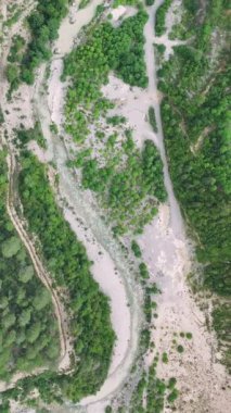 Yukarıdan, gür, ormanlı dağ vadisinin nefes kesici güzelliğini tecrübe edin. Dolambaçlı nehri takip et ve doğal güzellikler yeşil araziyi aydınlatırken izleri takip et.