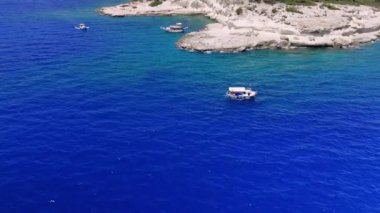 Turkuaz tekneler engebeli bir kıyı şeridi boyunca süzülüyor, kıyıya yakın yelken açıyor ve turistlere manzaranın tadını çıkaran manzaralı manzaralar sunuyor.