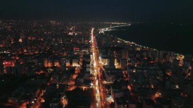 Kıyı kenti, karanlık Akdeniz 'e bitişik parıldayan binalar ve hareketli caddelere sahiptir. Arabalar kıyı yolu boyunca yol alırlar.