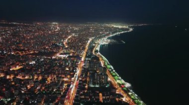 İzmir 'in kuş bakışı manzarası, hindi. Şehir sokak lambaları ve bina ışıklarıyla aydınlatılıyor. Ege denizi karanlıktır ve şehir ışıklarını yansıtır