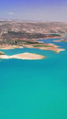 Turkuaz sular yaz boyunca açık mavi bir gökyüzünü yansıtırken, düşük su seviyeleri kuraklık ve iklim değişikliğinin etkilerini vurgulayarak gölün etrafındaki kuru araziyi ortaya çıkarır.