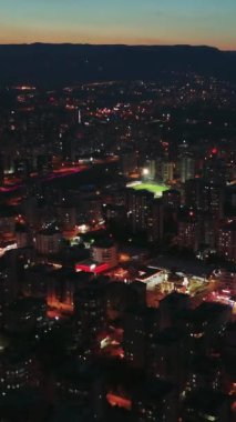 Kuşbakışı görüş, alacakaranlığa yenik düşen bir şehri yavaş yavaş yakalıyor. Güneş ufuktan batarken. Sokak lambaları ve bina ışıkları şehir manzarasını aydınlatıyor