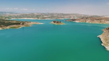 Turkuaz su berrak mavi bir gökyüzünün altında ışıldıyor, yemyeşil tepelerle çevrili. Huzurlu bir göl güneş ışığını yansıtır ve yaz kaçamakları için mükemmel bir manzara yaratır.