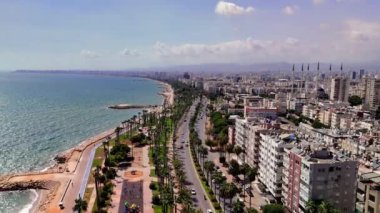 Türkiye 'de kıyı kenti olan Mersin' de, kıyı şeridi boyunca uzanan palmiye ağaçları ve Akdeniz 'in canlı maviliğinden oluşan bir hava manzarası sergileniyor.
