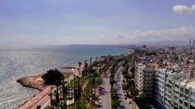 Mersin 'in sahil şehrinde kameralar canlı binalar, hareketli yollar ve tüylü bulutlarla dolu berrak mavi gökyüzünün altında çarpıcı bir Akdeniz gösteriyor.