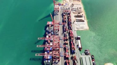 Vinçler nakliye konteynerlerini hareketli bir kargo terminalinde kaldırır ve hareket ettirir. Kargo gemileri, denizcilik lojistiğinin dinamik operasyonlarını gösteren yüklerini rıhtımlarda boşaltır.