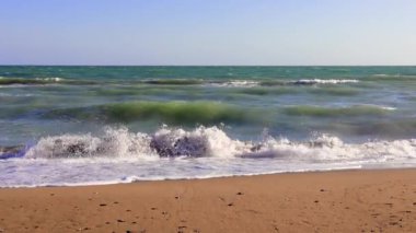 Tenha bir sahile çarpan turkuaz dalgalar sakin bir atmosfer yaratır. Açık mavi bir gökyüzü ve okyanusun rahatlatıcı sesi huzur ortamını güçlendirir.