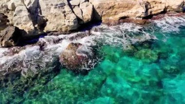 Turkuaz dalgalar kayalara çarparak güneşli bir günde beyaz köpük oluşturur. Şeffaf su deniz tabanını gözler önüne seriyor ve kıyı manzarasının güzelliğini arttırıyor.