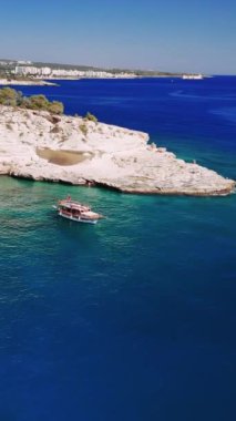 Küçük turist teknesi güneşli bir güneşin altında nefes kesen beyaz uçurumların yakınında dinleniyor. Turkuaz sular berraklıkla parıldar, rahatlama ve macera için ideal bir ortam yaratır.