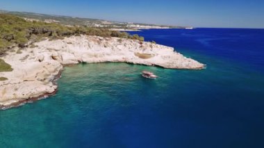 Küçük turist teknesi güneşli bir güneşin altında nefes kesen beyaz uçurumların yakınında dinleniyor. Turkuaz sular berraklıkla parıldar, rahatlama ve macera için ideal bir ortam yaratır.