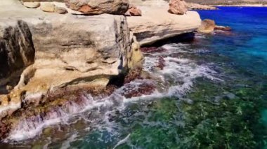 Turkuaz deniz suyu, parlak bir güneşin altındaki kayalara çarpıyor açık dalgalar okyanus tabanını ortaya çıkarıyor ve doğal güzelliklerle dolu çarpıcı bir sahil manzarası yaratıyor.