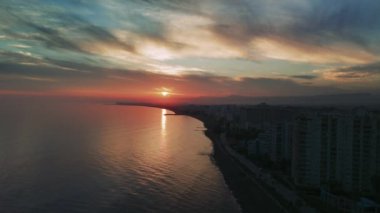 Sersemletici günbatımı, Akdeniz 'in üzerinde ılık bir parıltı yayar, suyu aydınlatır ve renkli gökyüzüne karşı kıyı şehirlerinin gökyüzünü görkemli bir şekilde görmesine neden olur.