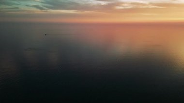 Küçük bir tekne, sakin bir Akdeniz 'de süzülerek hafif bir iz bırakır. Çarpıcı bir günbatımı gökyüzünü turuncu ve pembe renkli renklerle yıkar.