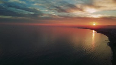 Güneş Akdeniz 'deki bir sahil kasabasında batıyor. Gökyüzü renkli bulutlarla dolu ve su gökyüzünün renklerini yansıtıyor.