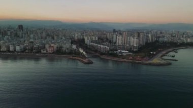 Mersin şehri kıyı ufkunu aydınlatıyor, alacakaranlık gökyüzüne karşı yükselen yerleşim kuleleri, şehir manzarasını akşam saatlerinde Akdeniz kıyılarıyla harmanlıyor.