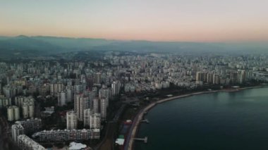 Mersin kıyısı şehir manzarası dağ manzarasını gözler önüne seriyor. Akdeniz şehirlerinin mimari güzelliklerini, alacakaranlıkta canlı pembe ve mavi gökyüzü renkleriyle sergiliyor.