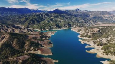 Hindideki güzel dağ gölü değişen ışığın ve yeryüzündeki gölgenin etkisini gözler önüne seriyor, açık mavi su gökyüzünü yansıtıyor ve yemyeşil ve kayalık arazilerle çevrili.