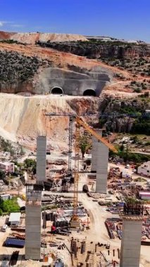 İnşaat işçileri kayalık araziyi kazıyor, yeraltı tüneli ve Türk kırsalında beton viyadük inşa ederken ağır makineler kullanıyor.